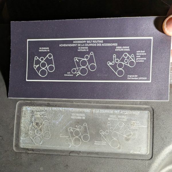 New serpentine belt routing label held next to the faded original on a 2002 Chevrolet Tahoe fan shroud